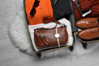 Photo of Open suitcase with folded clothes, accessories and shoes on floor, top view