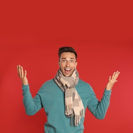 Photo of Excited young man in scarf and sweatshirt on red background. Winter season