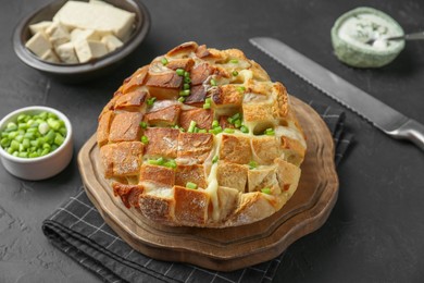 Freshly baked bread with tofu cheese, green onions and knife on black table