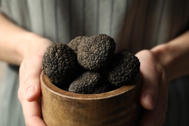 Photo of Woman holding wooden bowl of black truffles in hands, closeup