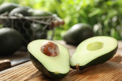 Photo of Halves of delicious ripe avocado on wooden board against blurred background