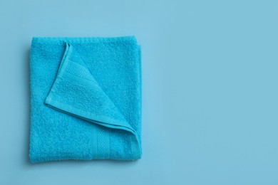 Photo of Folded soft beach towel on light blue background, top view. Space for text