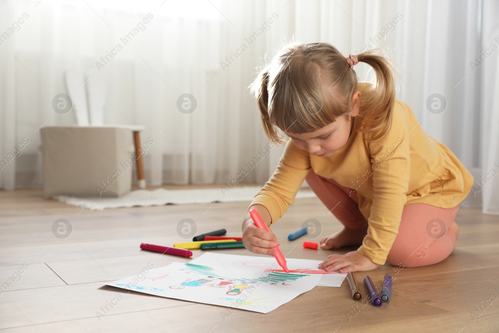 Photo of Cute little girl drawing with marker on floor indoors. Child`s art