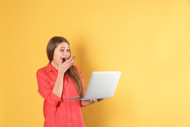 Emotional young woman with laptop celebrating victory on color background. Space for text