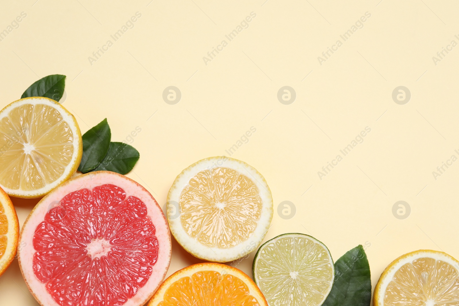 Photo of Different cut citrus fruits and leaves on beige table, flat lay. Space for text