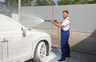 Photo of Young worker cleaning automobile with high pressure water jet at car wash