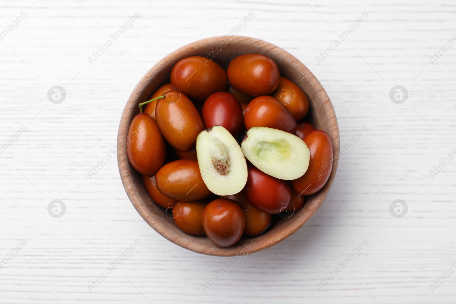 Photo of Fresh Ziziphus jujuba fruits in bowl on white wooden table, top view