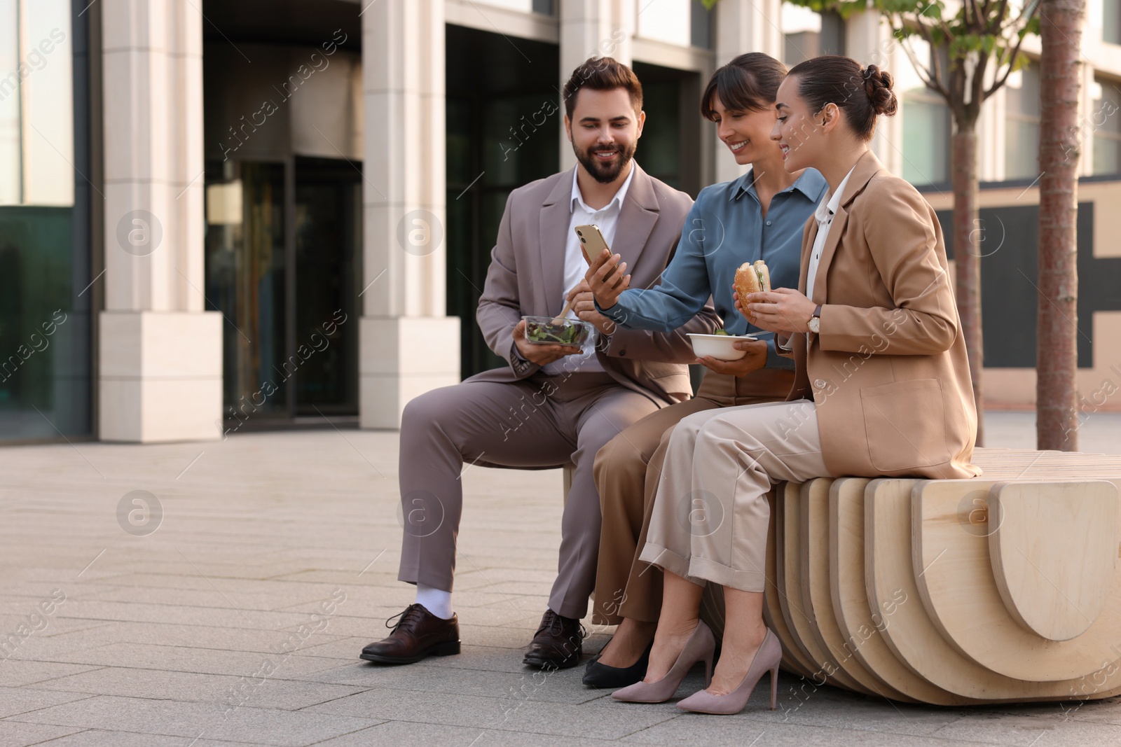 Photo of Business lunch. Happy colleagues spending time together during break on bench outdoors