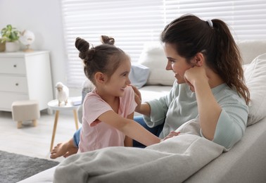 Photo of Young mother and her daughter spending time together on sofa at home