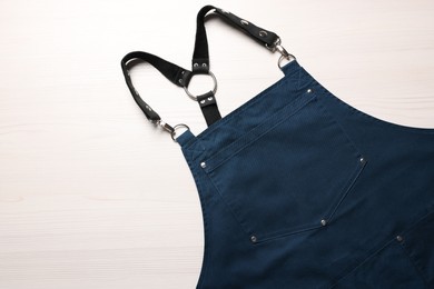 Photo of Stylish dark blue apron on white wooden table, top view. Mockup for design