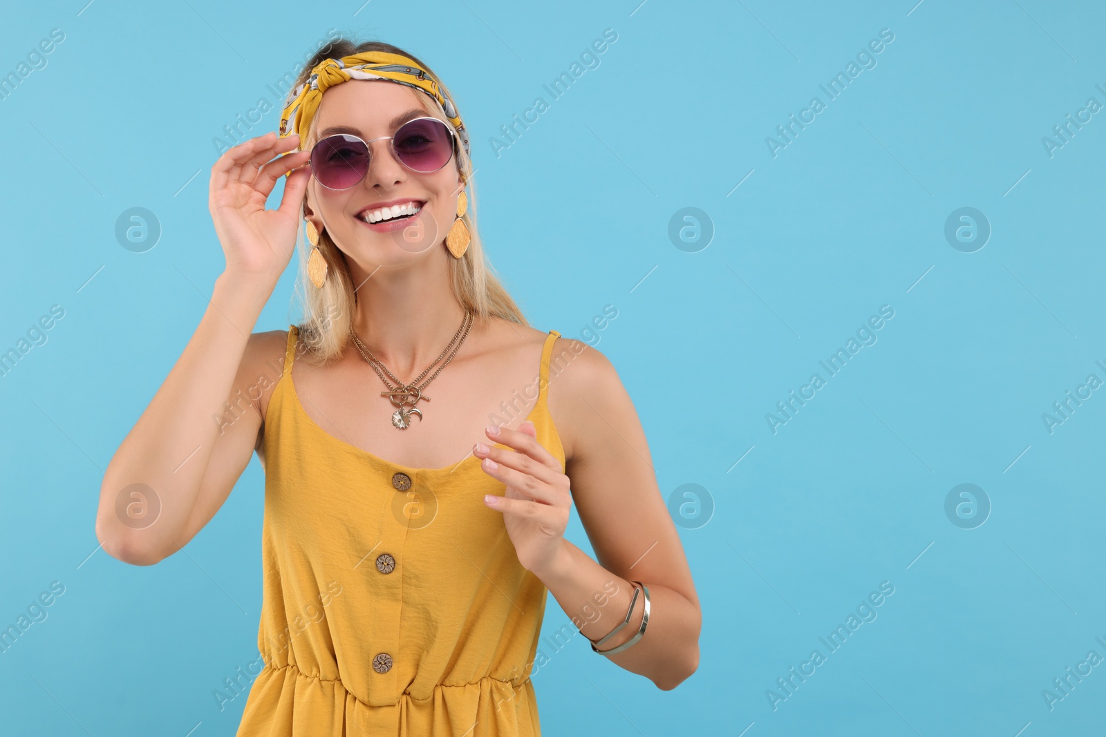 Photo of Portrait of smiling hippie woman in sunglasses on light blue background. Space for text