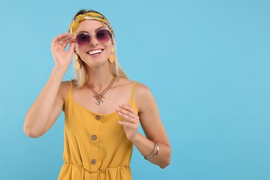 Portrait of smiling hippie woman in sunglasses on light blue background. Space for text