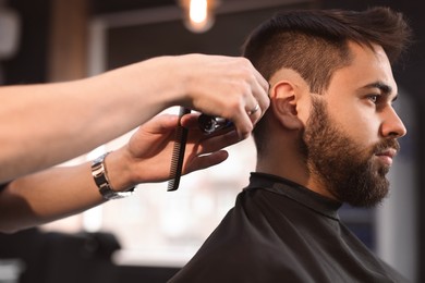 Professional hairdresser working with client in barbershop