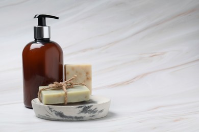 Photo of Soap bars and bottle dispenser on light marble background, space for text