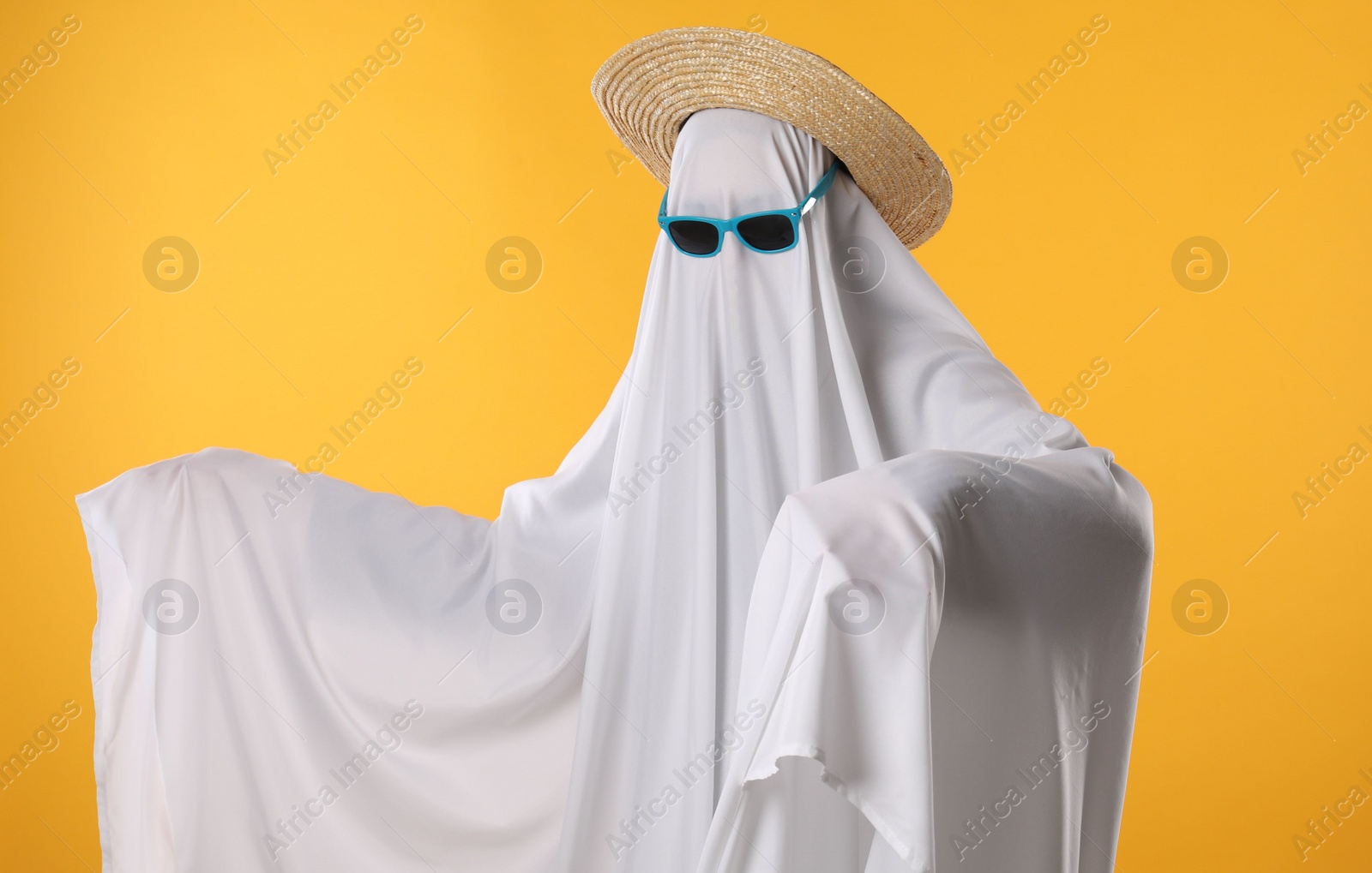 Photo of Person in ghost costume, sunglasses and straw hat on yellow background