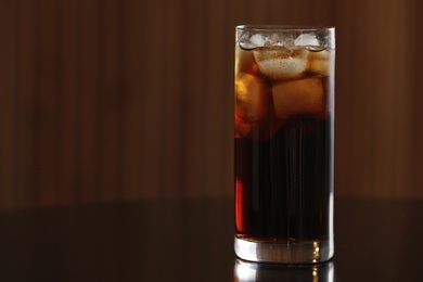 Photo of Glass of cola with ice on table against blurred background. Space for text