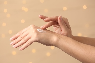 Woman applying hand cream on blurred background, closeup