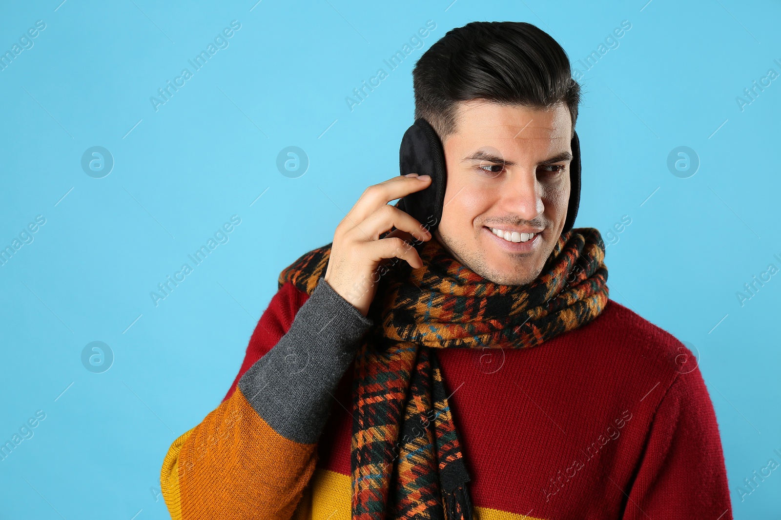 Photo of Man wearing stylish earmuffs and scarf on light blue background
