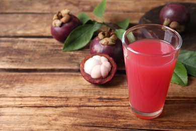 Delicious fresh mangosteen juice in glass on wooden table, space for text