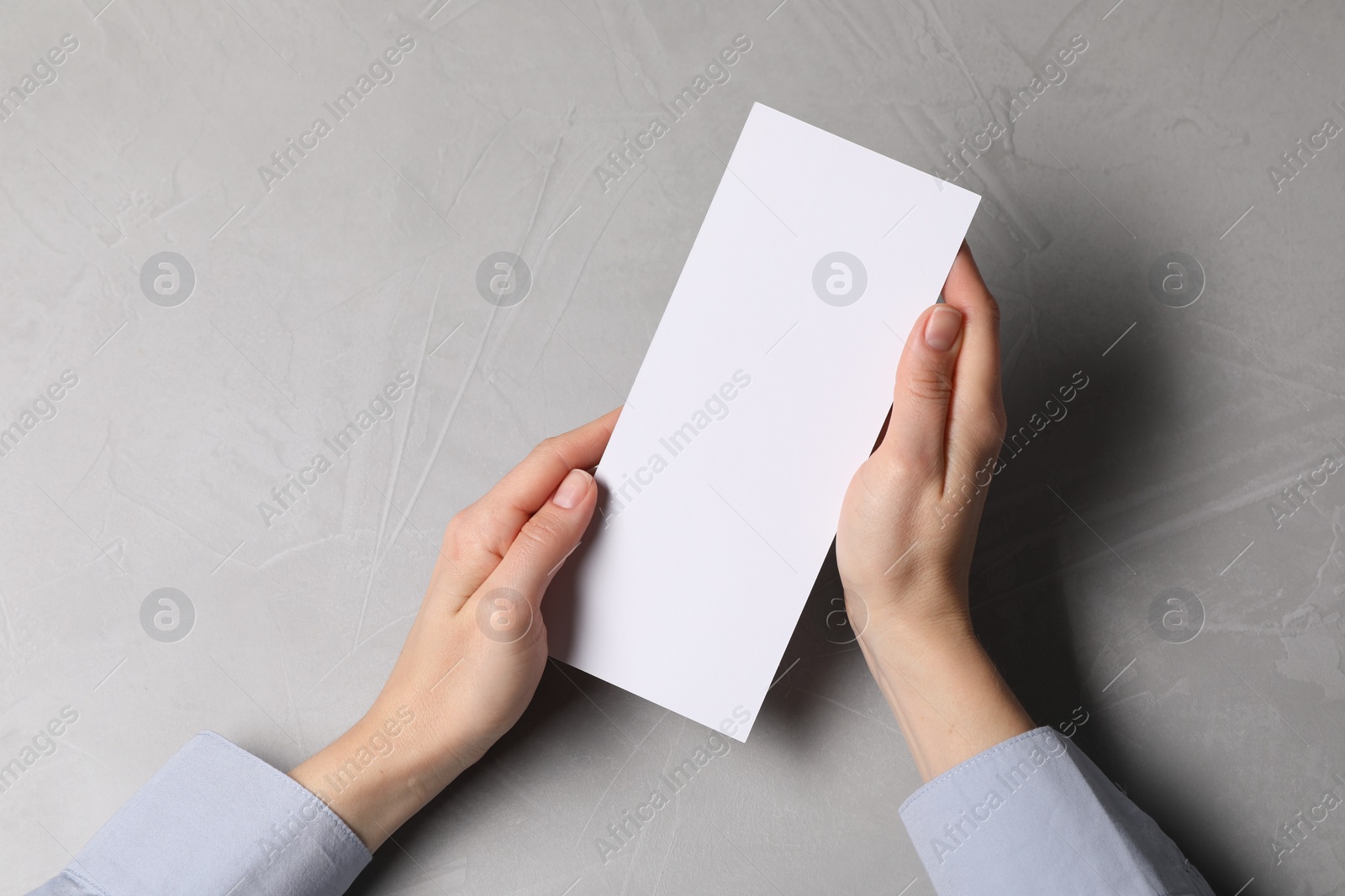 Photo of Woman holding blank card at light grey table, top view. Mockup for design