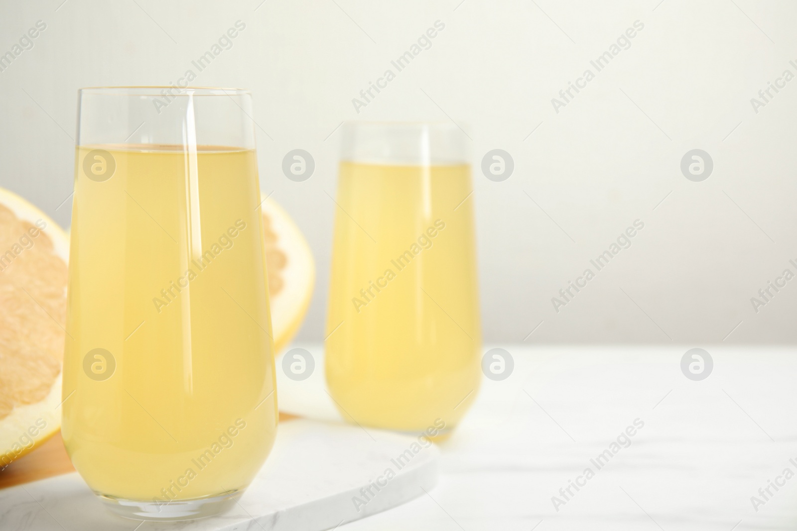 Photo of Glasses of fresh pomelo juice on white table. Space for text