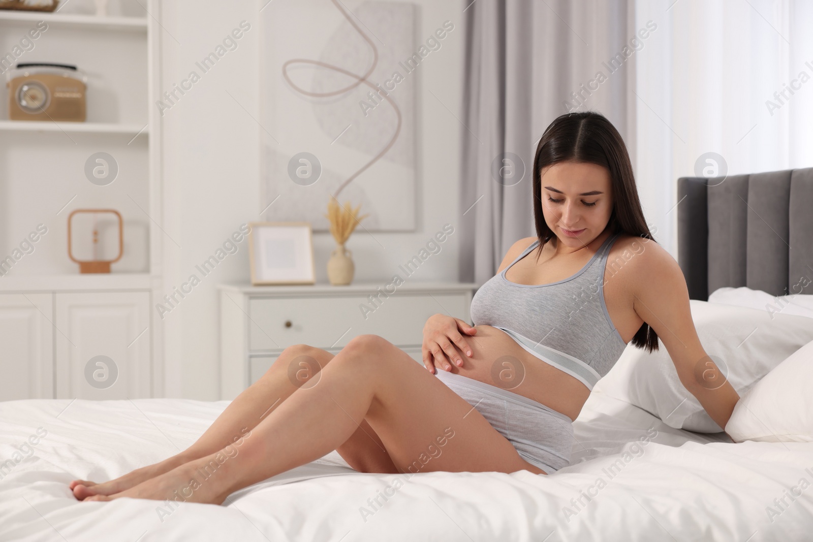 Photo of Beautiful pregnant woman in comfortable maternity underwear on bed at home