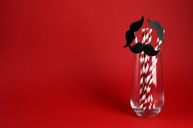 Photo of Fake paper mustaches and party props in glass on red background. Space for text