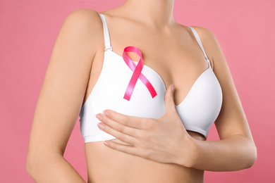 Woman with pink ribbon on color background, closeup. Breast cancer awareness