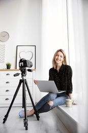 Photo of Young blogger with laptop recording video near window at home