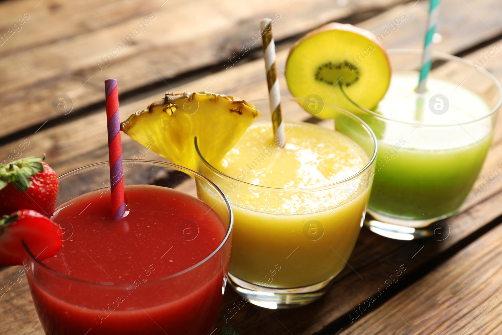 Photo of Delicious colorful juices in glasses on wooden table, closeup