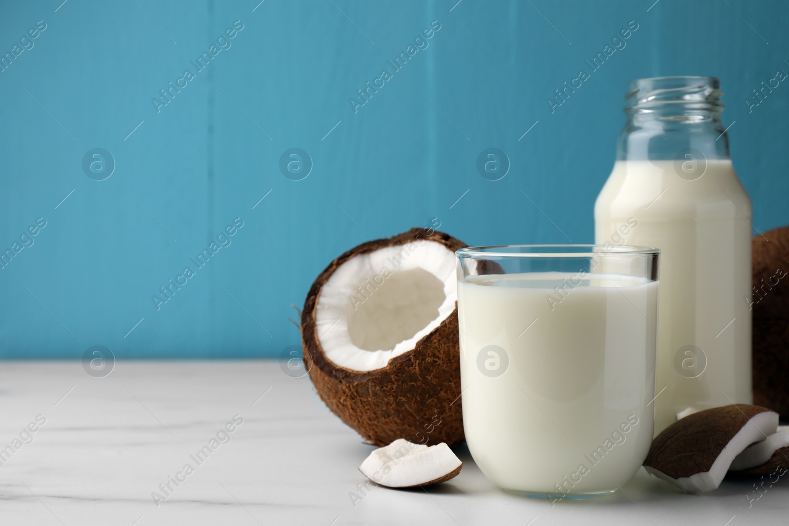 Photo of Glass and bottle of delicious vegan milk with coconuts on white marble table. Space for text