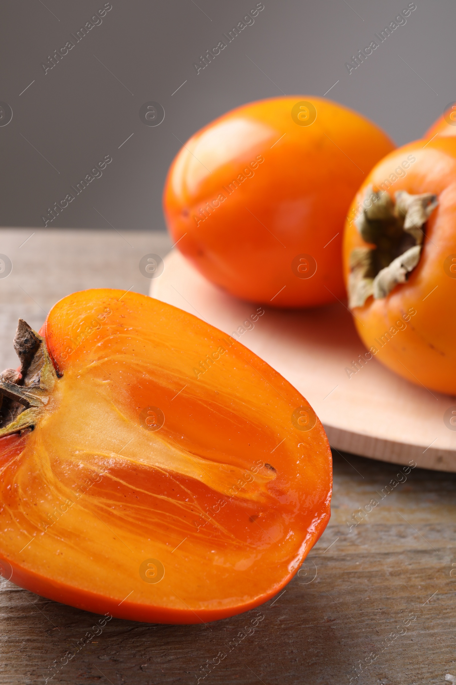 Photo of Whole and cut delicious ripe persimmons on wooden table, closeup