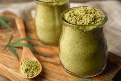 Photo of Jars of hemp protein powder on wooden board, closeup. Space for text