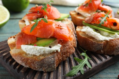 Photo of Delicious sandwiches with cream cheese, salmon, avocado and arugula on wooden board, closeup