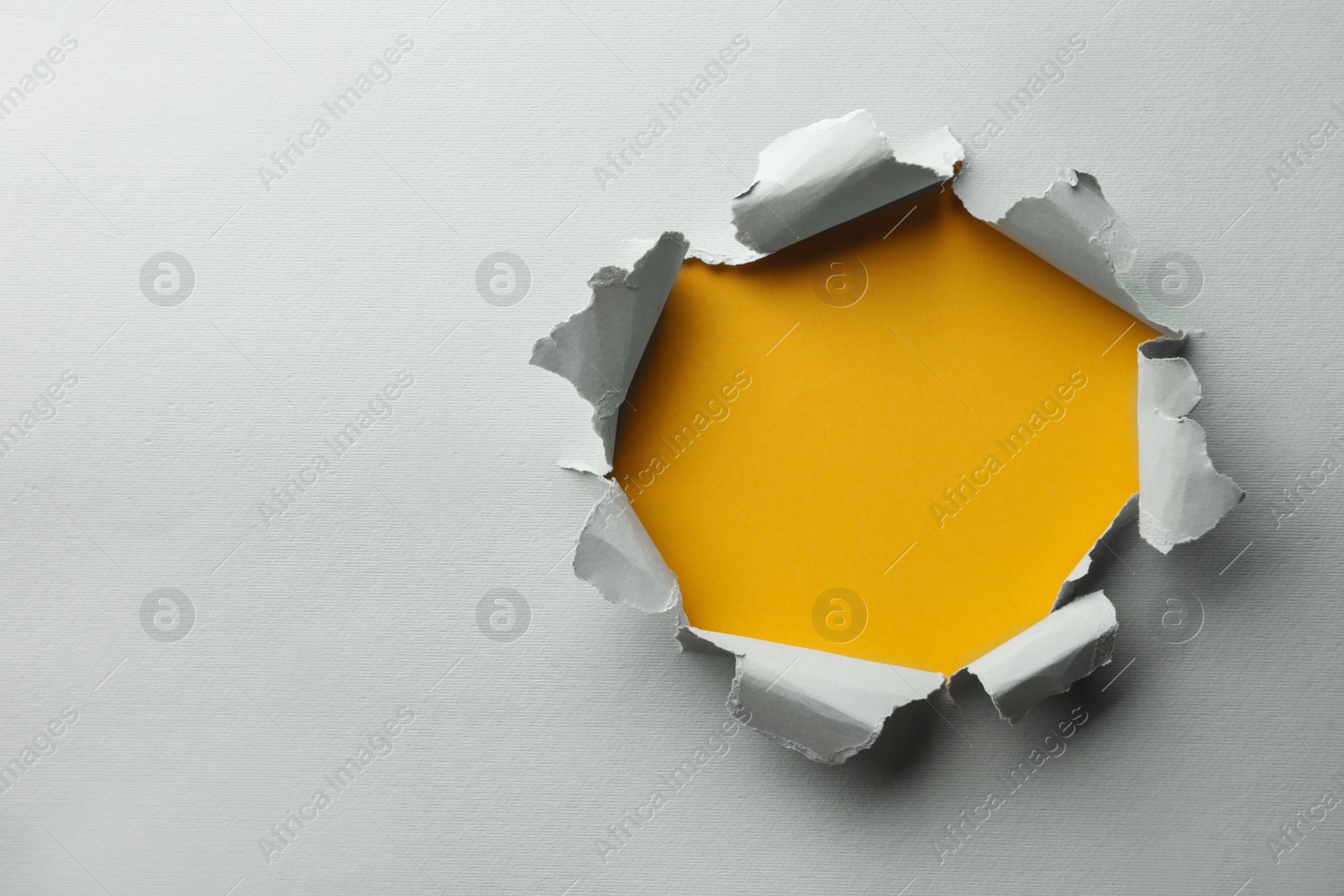 Photo of Hole in white paper on yellow background, space for text