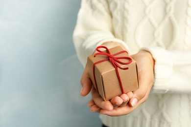 Photo of Woman holding beautiful Christmas gift on light blue background, closeup