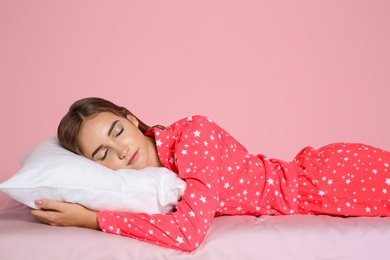 Beautiful teen girl sleeping with comfortable pillow on bed against color background