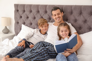 Photo of Father reading book with children in bedroom. Happy family