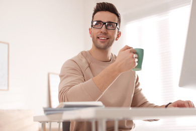 Photo of Young man with cup of drink relaxing at table in office during break