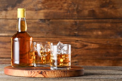 Whiskey with ice cubes in glasses and bottle on wooden table, closeup. Space for text