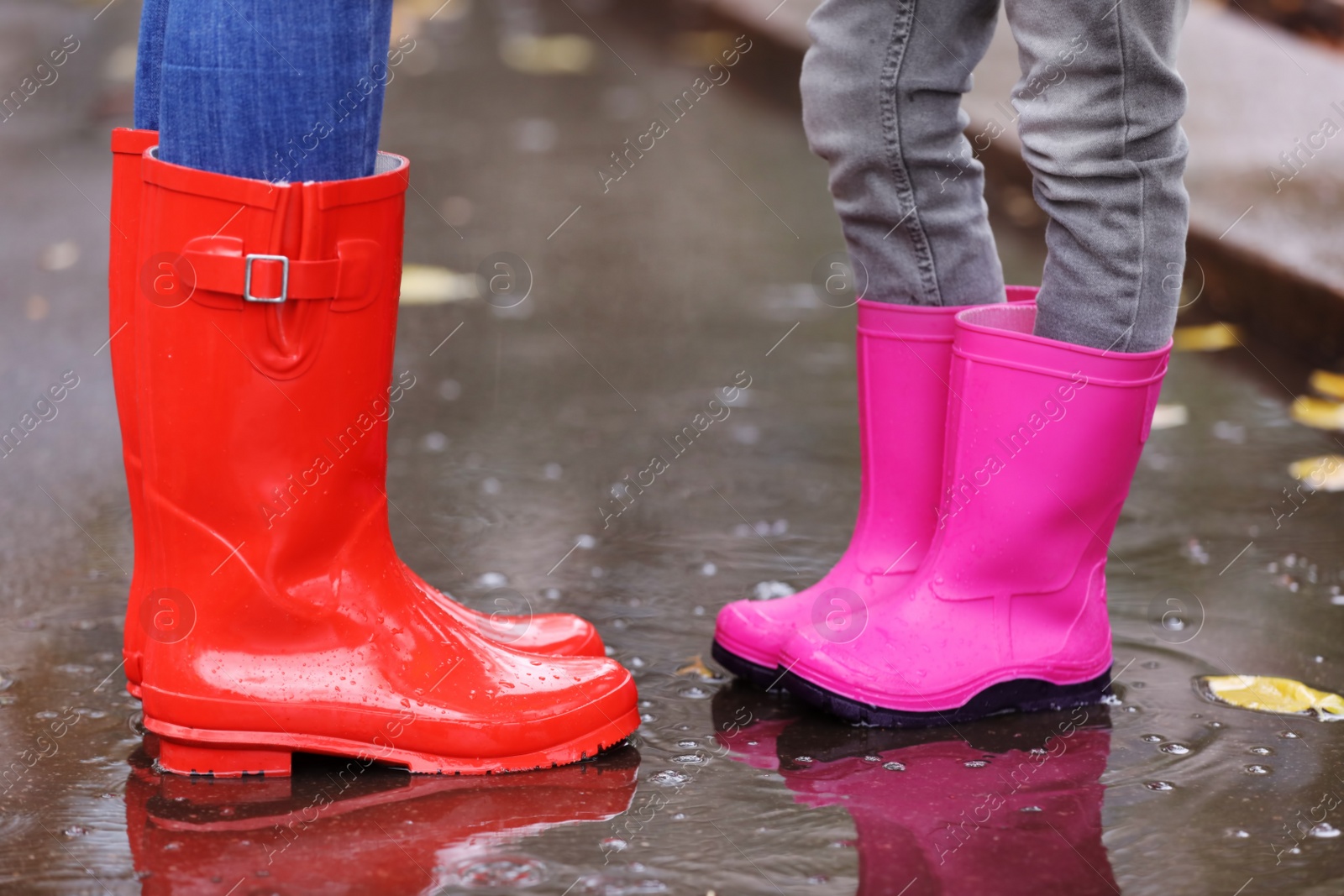 Photo of Mother and daughter wearing rubber boots standing in puddle on rainy day, focus of legs. Autumn walk