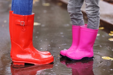 Mother and daughter wearing rubber boots standing in puddle on rainy day, focus of legs. Autumn walk