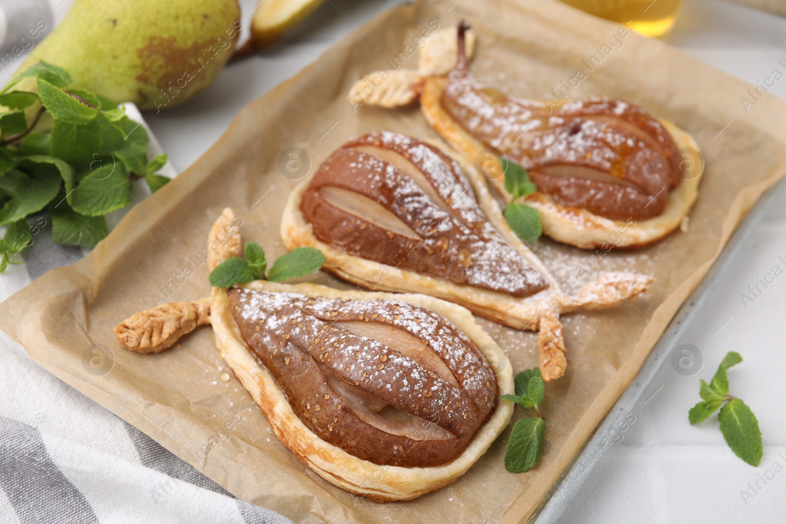 Photo of Delicious pears baked in puff pastry with powdered sugar and mint on white table, closeup