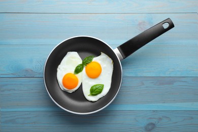 Tasty fried eggs in pan on light blue wooden table, top view