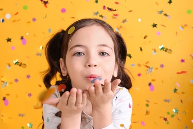 Photo of Adorable little girl blowing confetti on yellow background