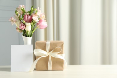 Photo of Happy Mother's Day. Gift box, blank card and bouquet of beautiful flowers in vase on white table indoors. Space for text