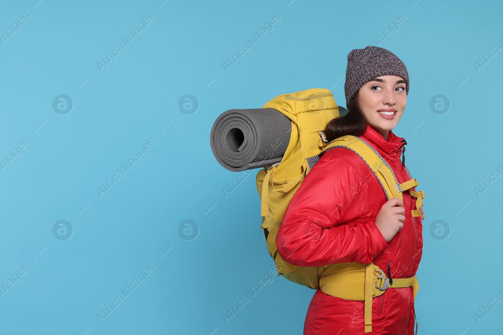 Photo of Smiling young woman with backpack on light blue background, space for text. Active tourism