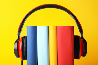 Photo of Books with modern headphones on yellow background, closeup