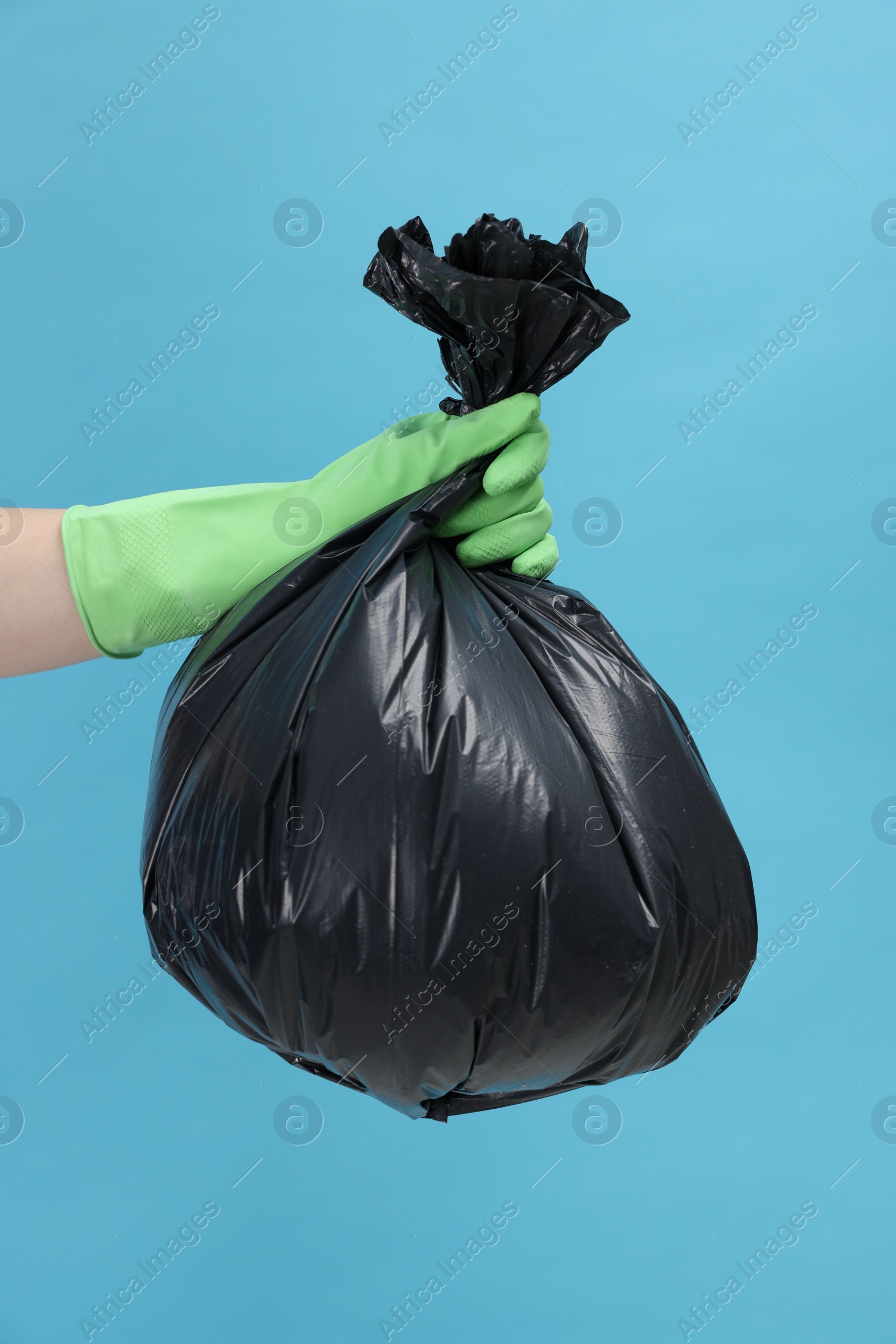 Photo of Woman holding plastic bag full of garbage on light blue background, closeup