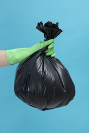 Photo of Woman holding plastic bag full of garbage on light blue background, closeup